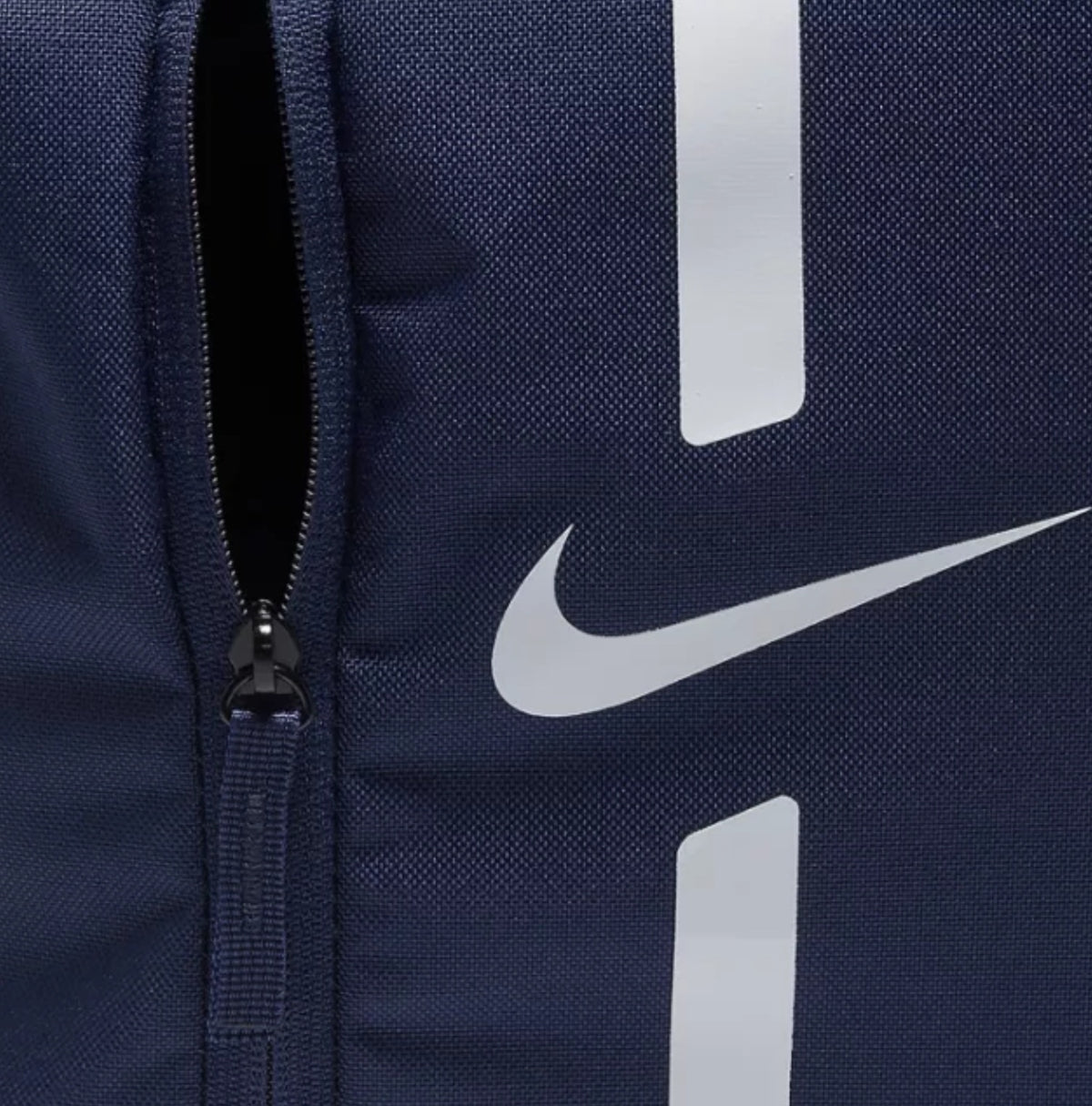 Close-up of a navy blue Nike Rucksack backpack featuring a white reflective Swoosh logo and vertical reflective stripes next to a black zipper.